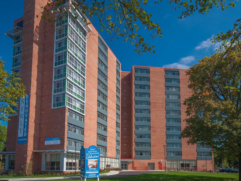 A tall brick apartment building with large windows against a clear blue sky.