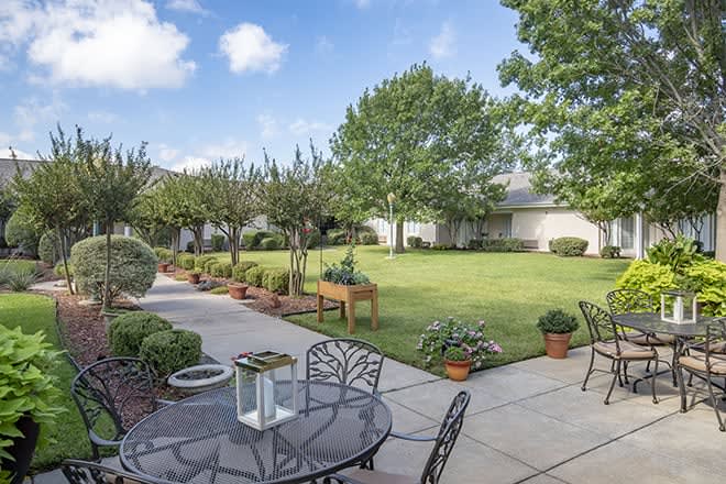 A serene backyard garden with a patio, outdoor furniture, and lush greenery.