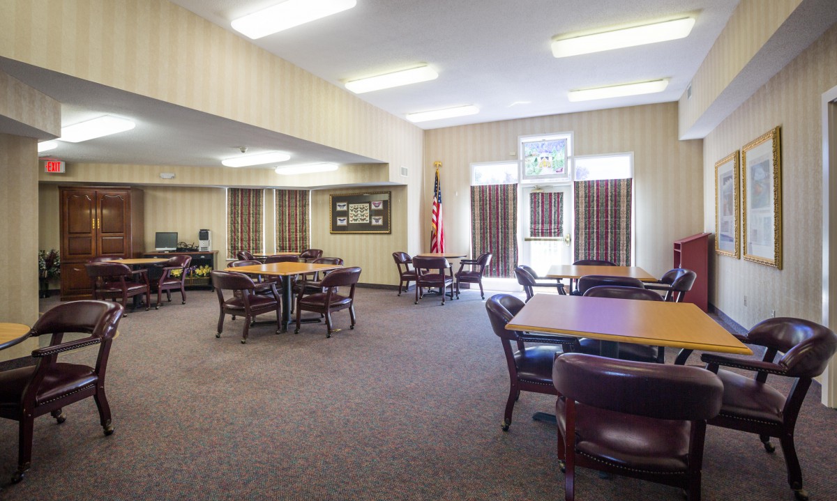 A spacious meeting room with tables and chairs, featuring curtains and an American flag.