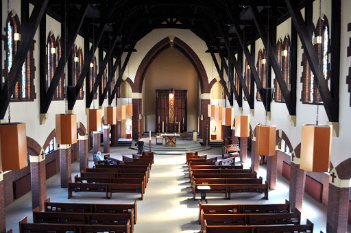 A serene view of a church interior featuring wooden beams and rows of pews.