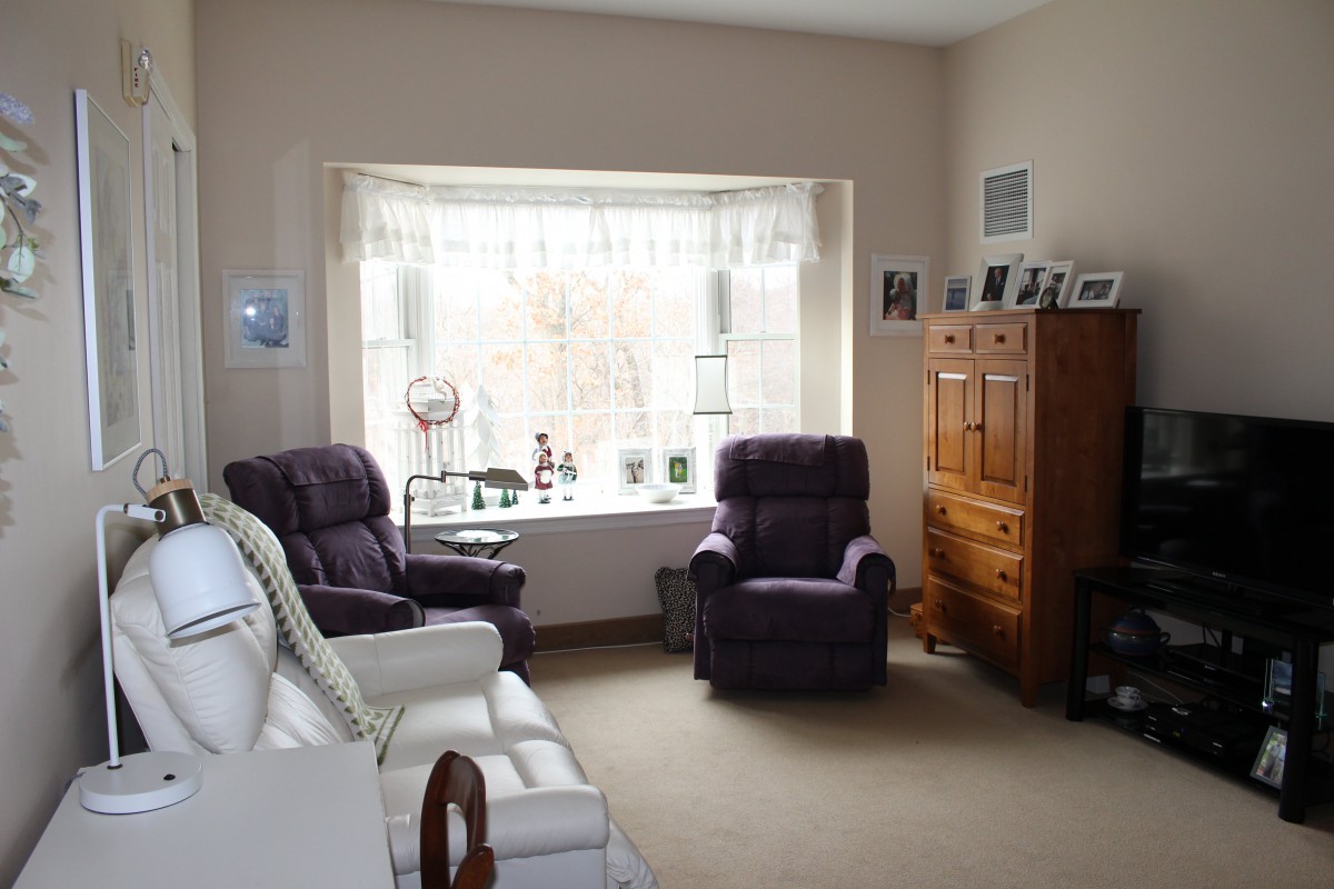 A cozy living room with comfortable chairs, a large window, and a wooden cabinet.