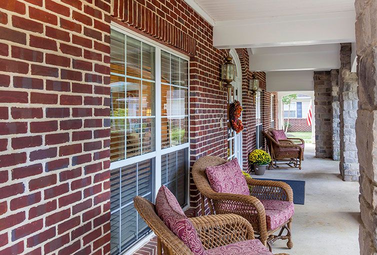 A cozy porch with wicker chairs and cushions against a brick wall.