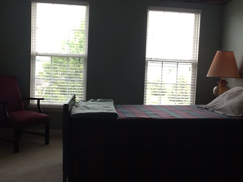 A cozy bedroom with a bed, two windows, a lamp, and a chair.