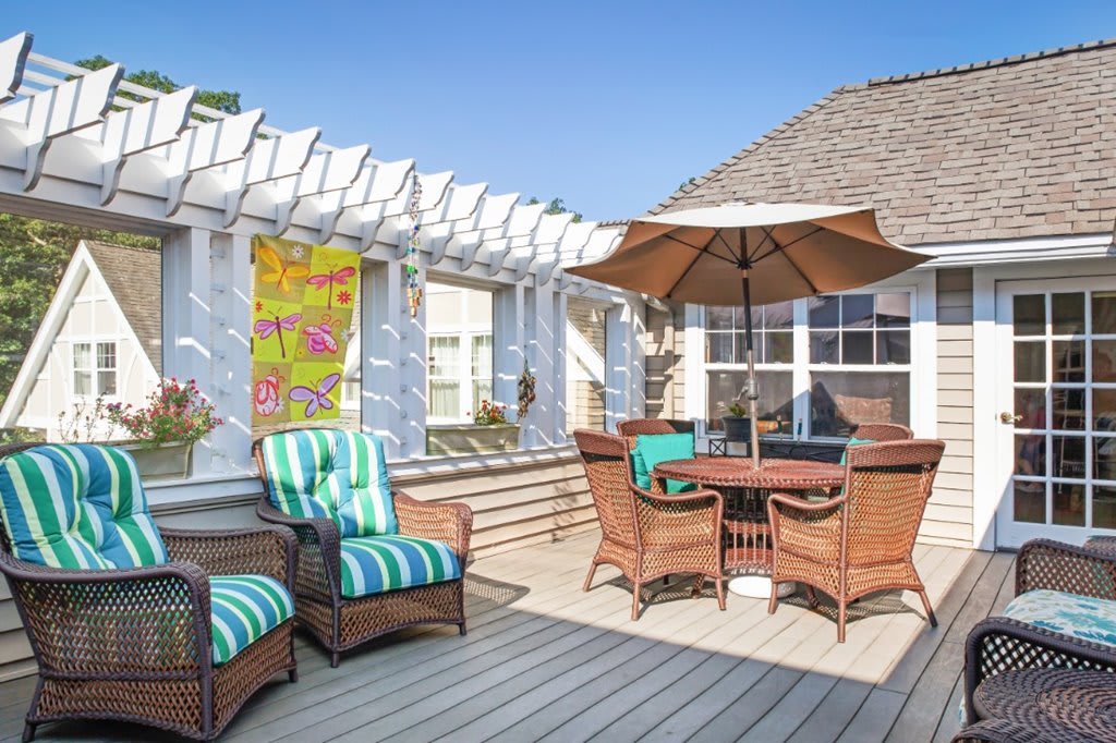 A sunny outdoor deck with wicker furniture and a large umbrella.