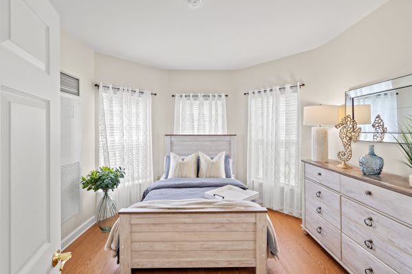 A cozy bedroom with neutral tones, featuring a well-made bed, elegant curtains, and ample natural light.