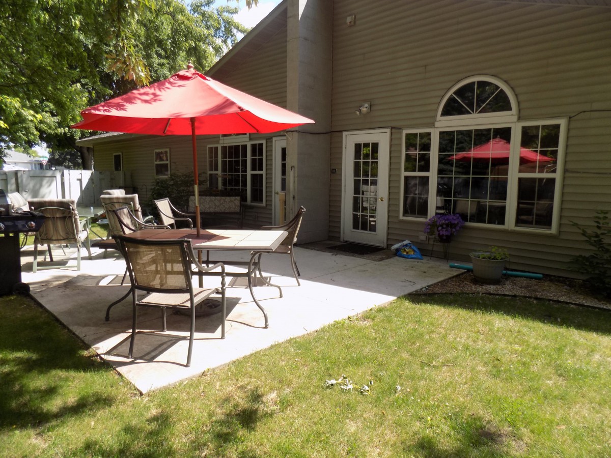 A cozy backyard patio featuring a red umbrella, outdoor table, and chairs on a sunny day.