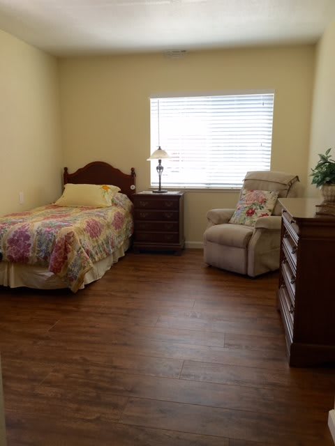 A simple bedroom with a single bed, dresser, and cozy chair by the window.