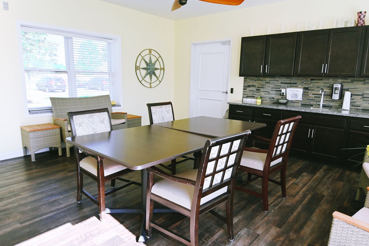 A cozy dining room with a dark wooden table and chairs, featuring a small kitchen area in the background.