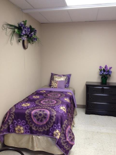A minimalist bedroom with a single bed adorned in purple patterned bedding and matching floral decor.