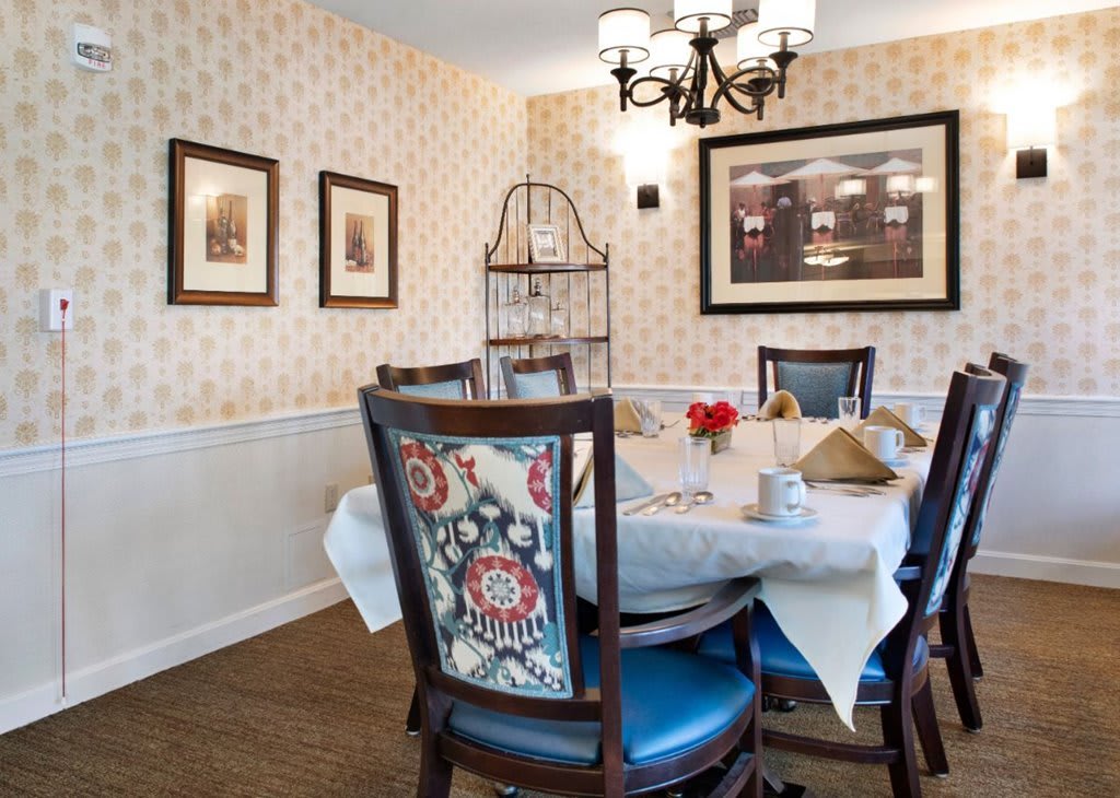 An elegantly decorated dining room with a round table and upholstered chairs under a chandelier.