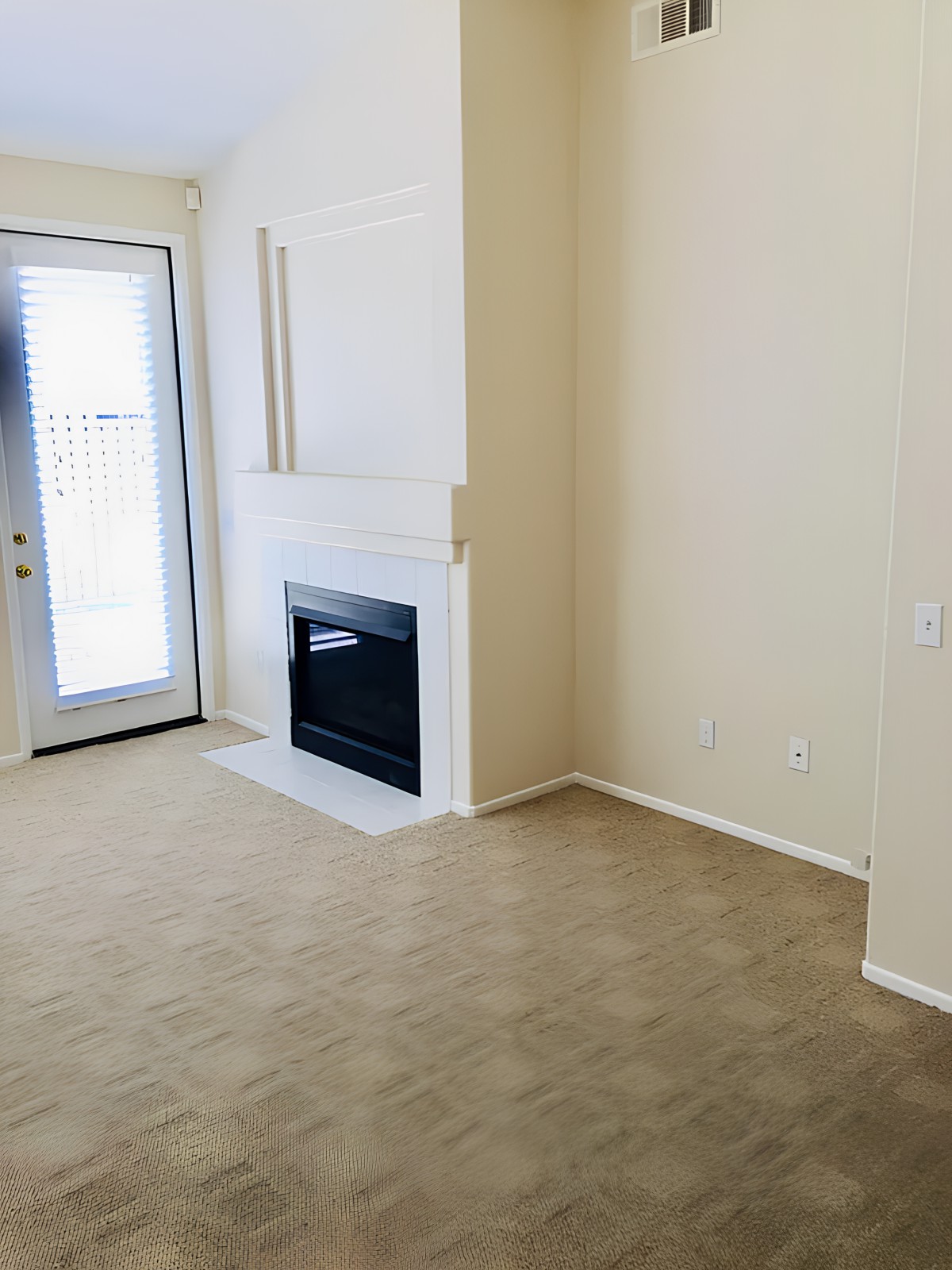 A cozy empty room featuring a fireplace, carpeted floor, and a door leading outside.