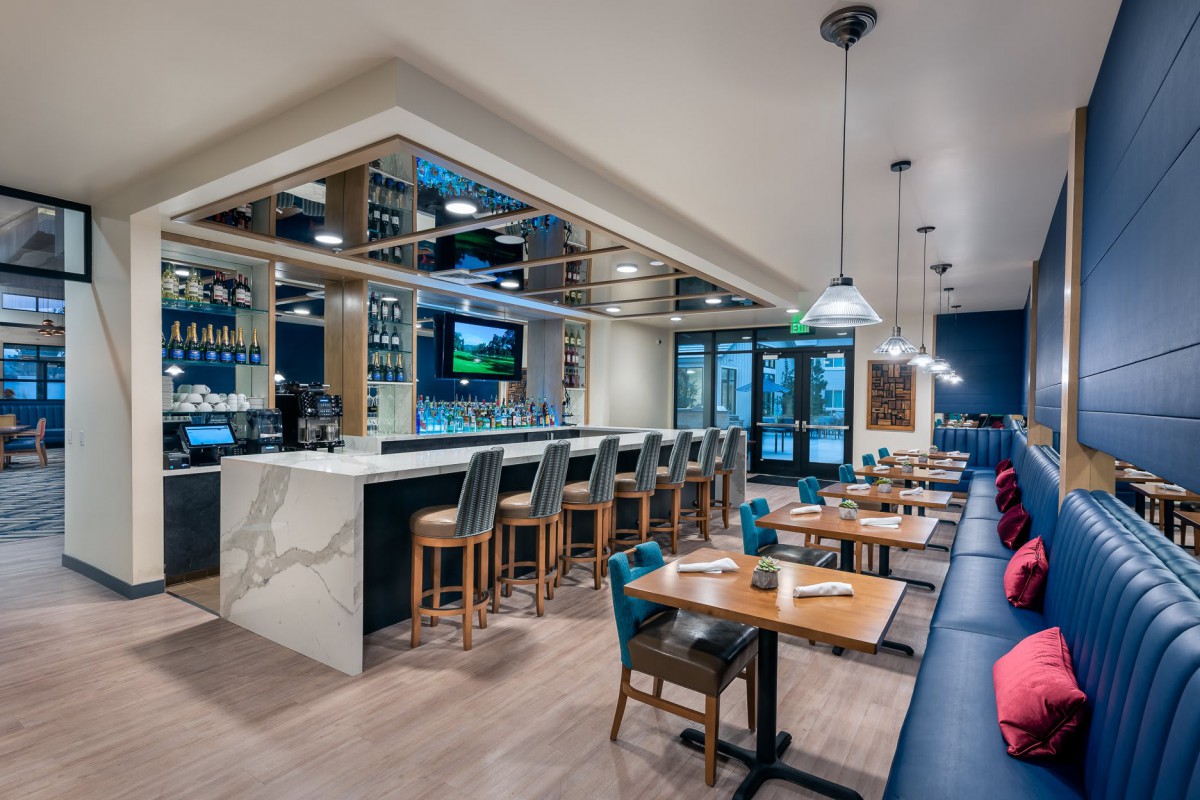 A modern restaurant interior featuring a sleek bar and a stylish dining area with wooden tables and chairs.