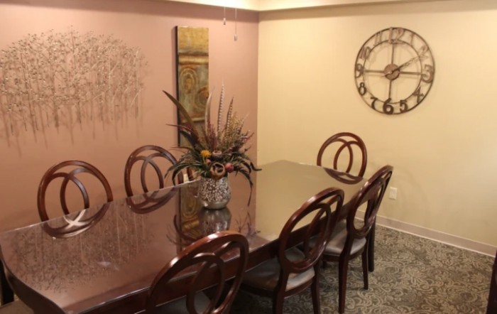A well-decorated dining room featuring a glass table with six chairs, wall art, and a large decorative clock.