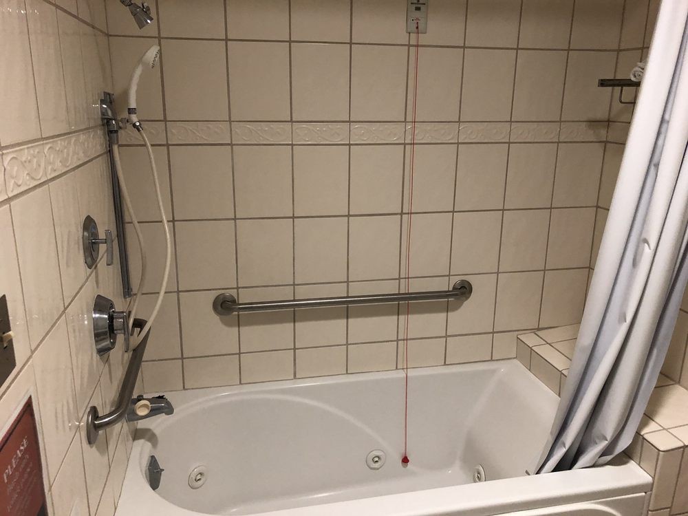 A bathroom featuring a bathtub with a showerhead and grab bar against tiled walls.