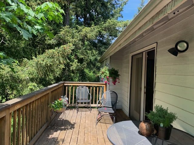 A cozy outdoor deck with seating, surrounded by lush greenery and plants.