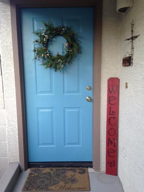 A blue front door adorned with a wreath and a red welcome sign.