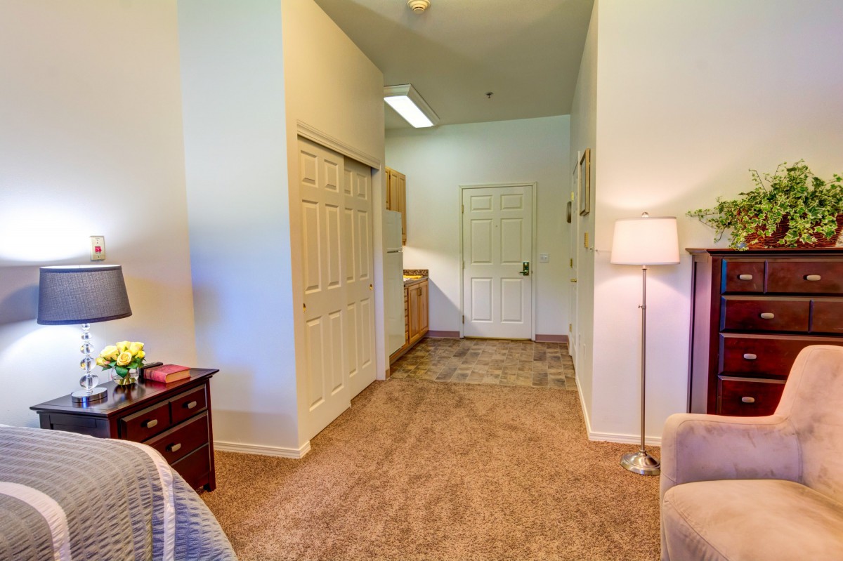 A carpeted hallway with a door, closet, and furniture including a lamp.