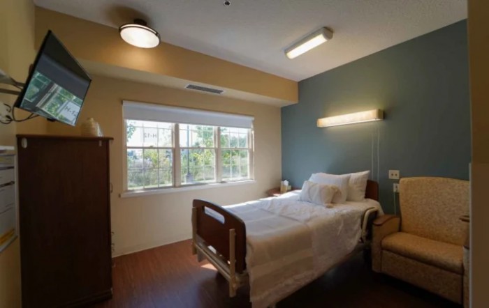 A quiet hospital room with a single bed, nightstand, and window.