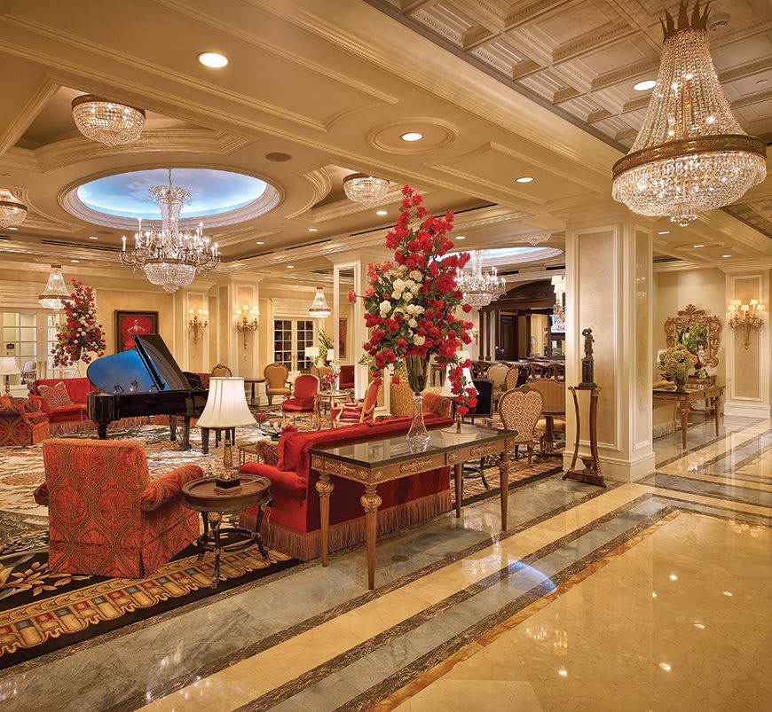 A lavishly decorated hotel lobby with chandeliers, a grand piano, and elegant furnishings.
