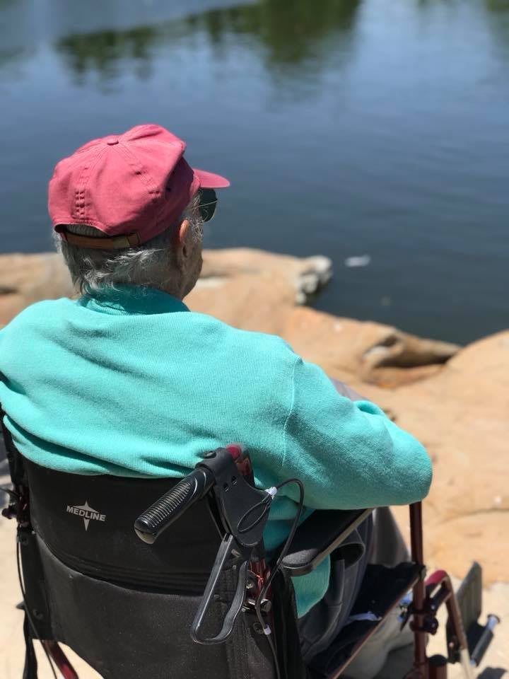 An elderly person in a wheelchair enjoys a scenic view by the lake.