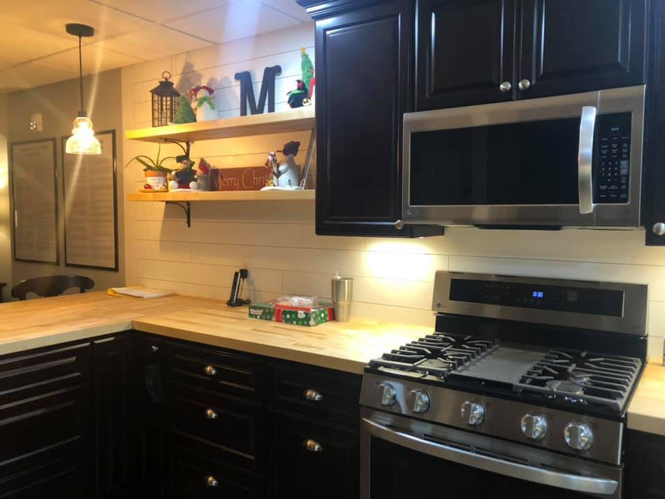 A cozy kitchen with dark cabinets, a stainless steel stove and microwave, and decorative shelving.
