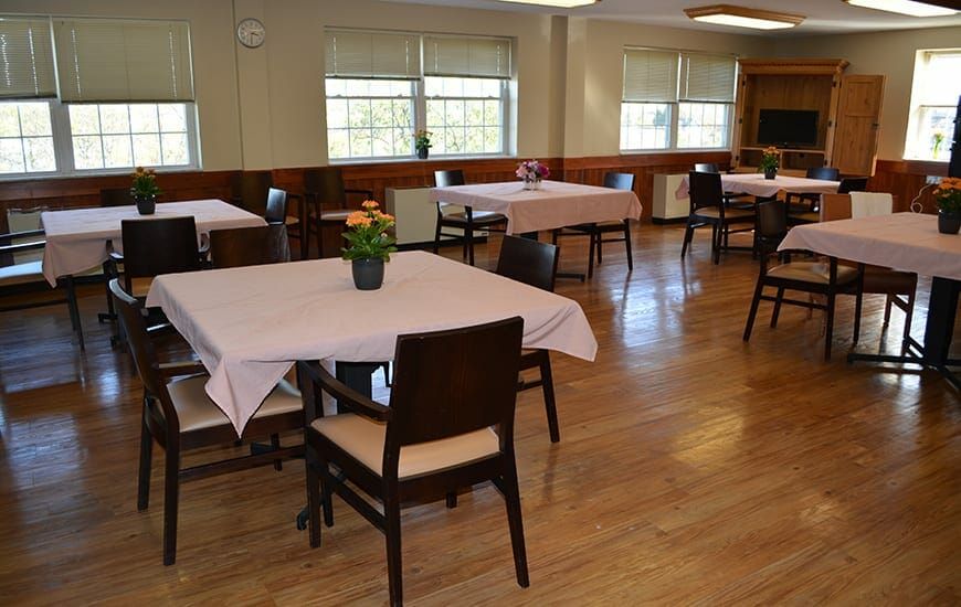 A spacious dining room with neatly arranged tables and chairs, adorned with tablecloths and potted plants.