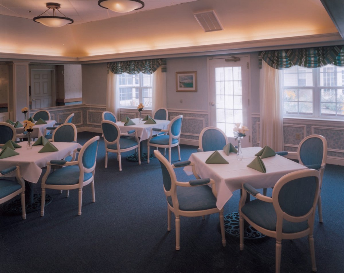 A well-lit dining room with elegantly set tables and blue upholstered chairs.