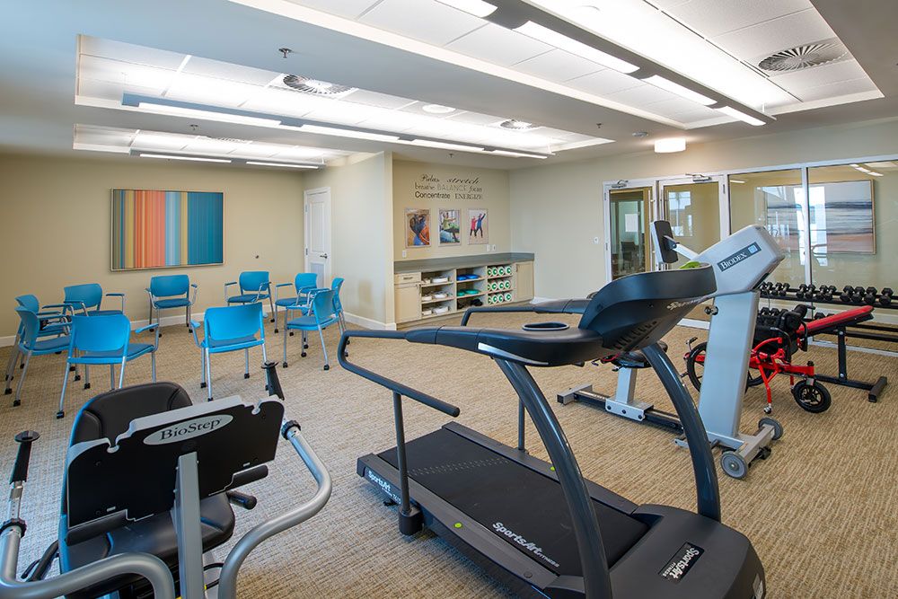 A modern fitness center with exercise equipment and chairs in a bright, spacious room.
