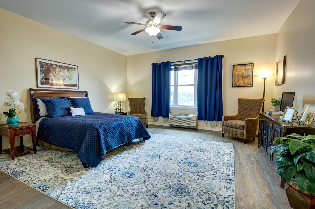 A spacious bedroom with blue accents, featuring a large bed, cozy seating area, and natural light.