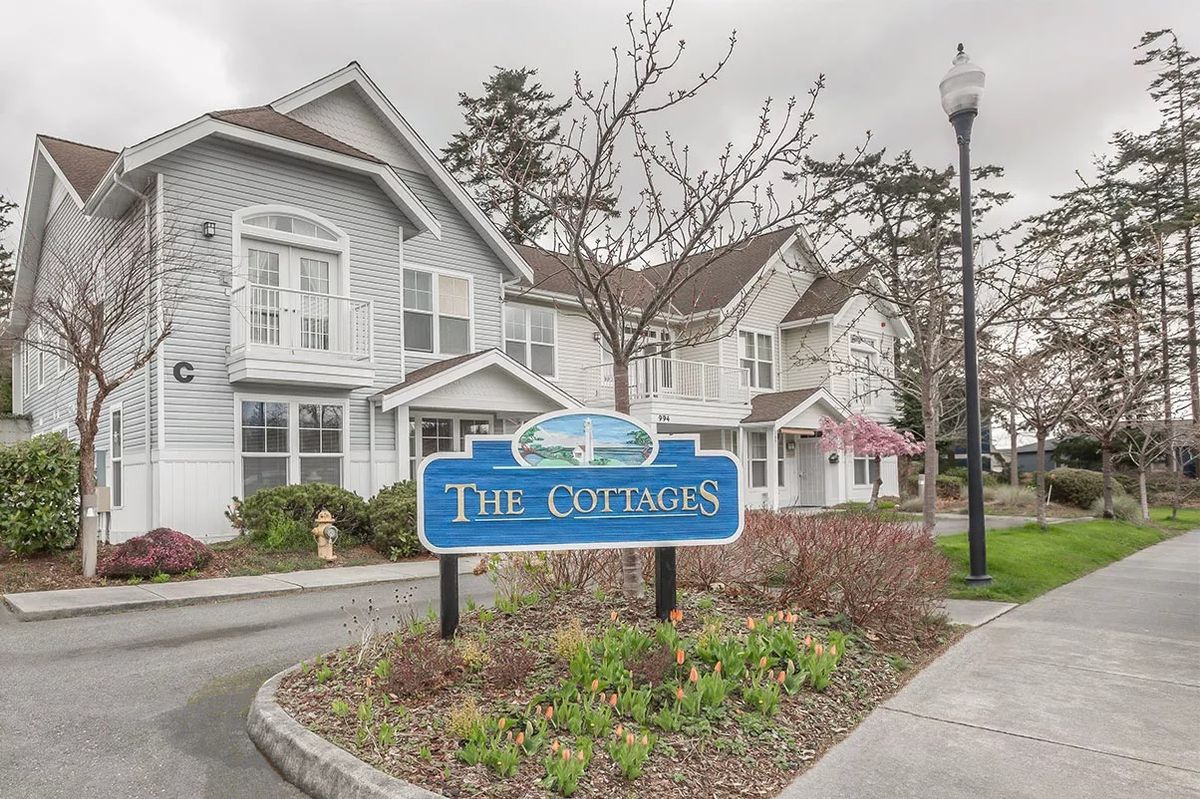 A residential area featuring a sign for 'The Cottages' with manicured landscaping and overcast skies.