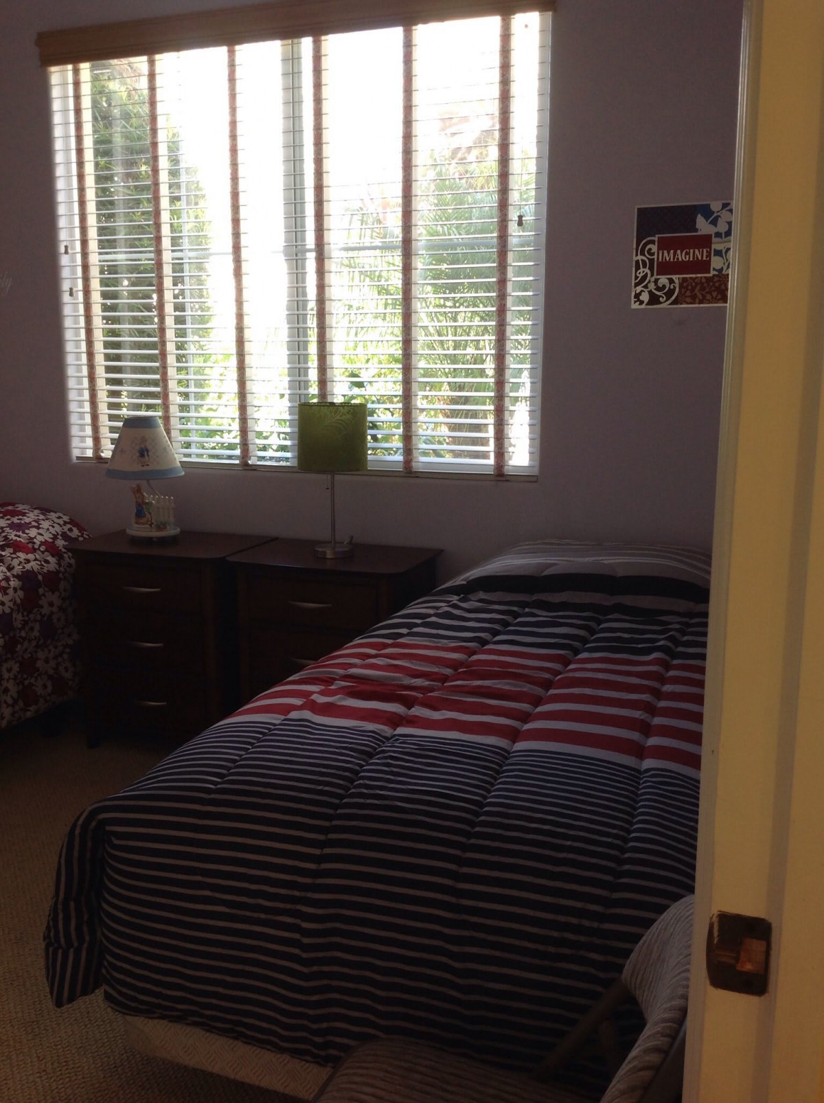 A cozy bedroom with a bed, side table, and window with blinds.