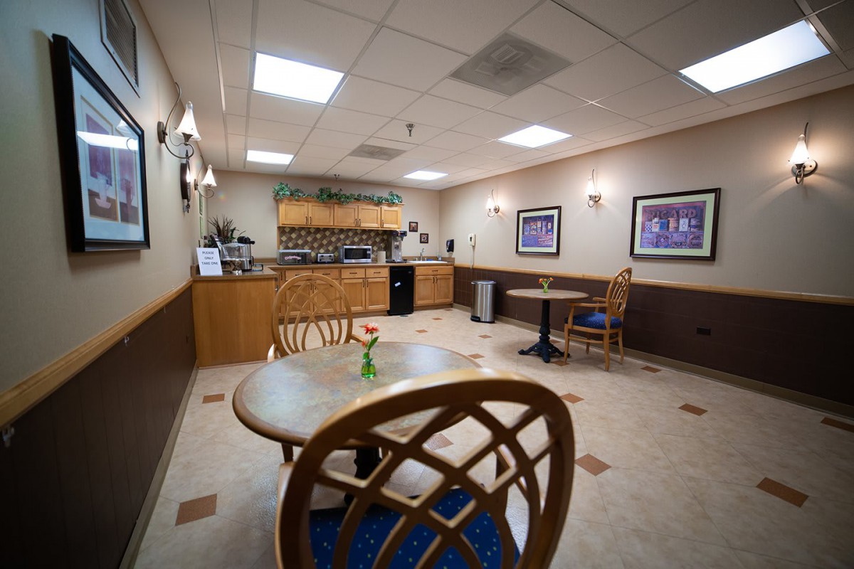 A cozy waiting room with tables and chairs, lit by ceiling lights and adorned with artwork on the walls.