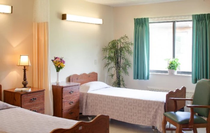 A cozy, well-lit bedroom featuring twin beds, wooden furniture, and a floral arrangement.