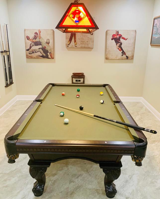 A stylish indoor game room featuring a pool table with a cue stick, balls arranged for play, and framed sports-themed artwork on the walls.