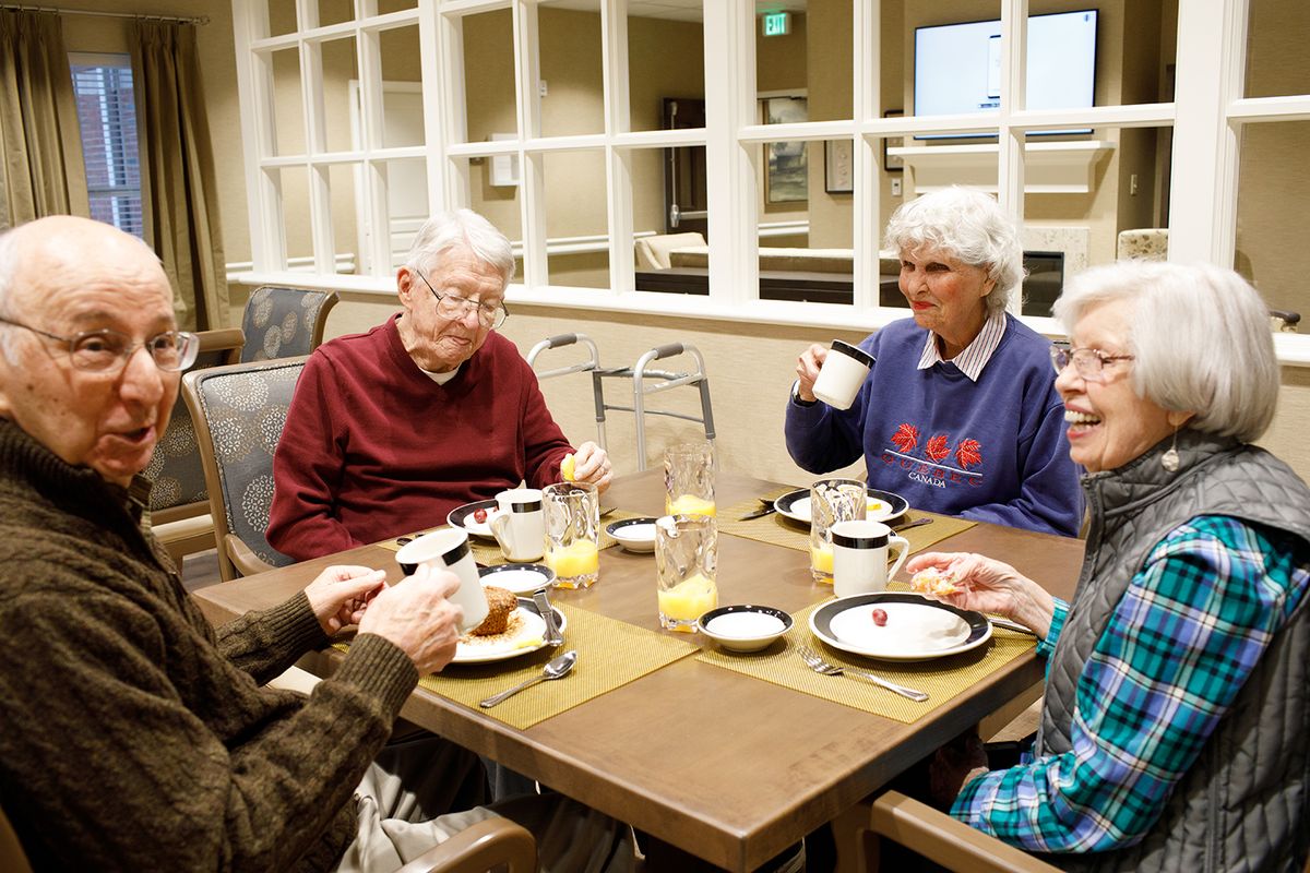 A group of elderly friends enjoying a meal and conversation indoors.
