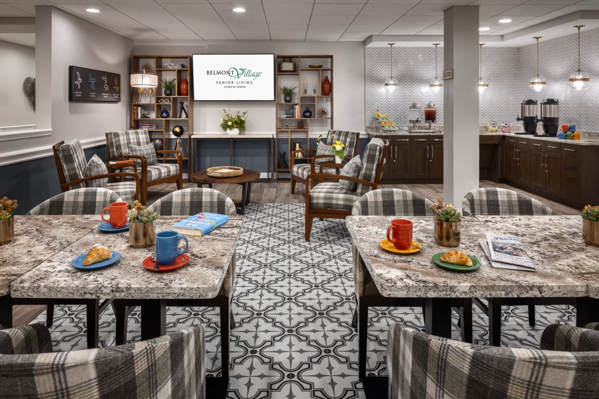 A stylish and comfortable meeting room with patterned carpet, tables set with colorful mugs, and upholstered chairs facing a projector screen.