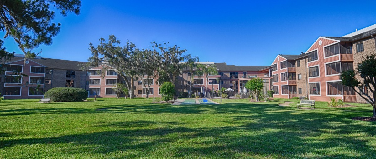 A view of an apartment building with a large grassy area and trees under a clear blue sky.