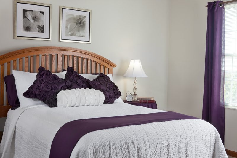 A cozy bedroom with a neatly made bed featuring purple accents and framed artwork on the wall.
