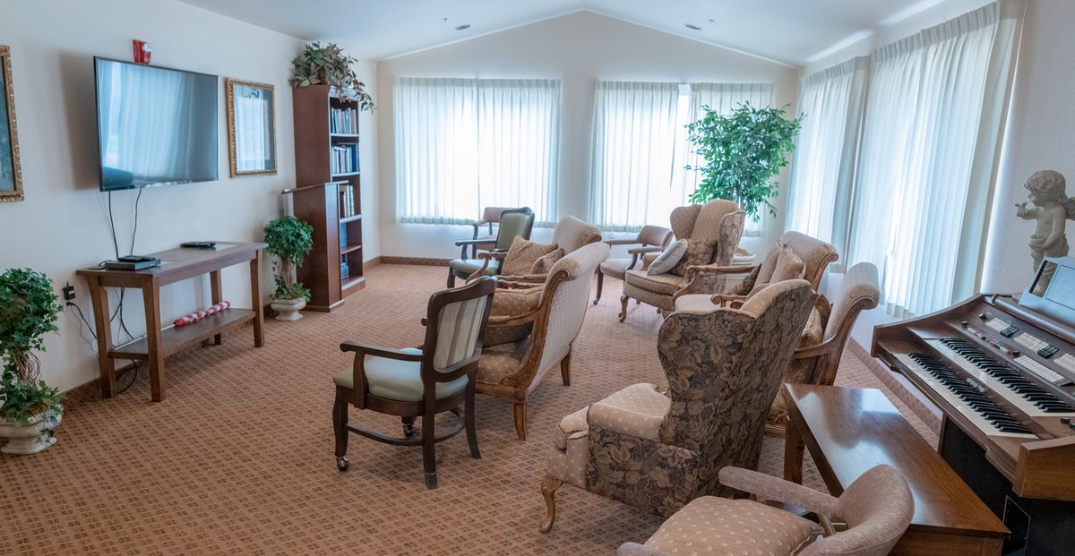 A spacious living room with multiple chairs, large windows, and a carpeted floor.