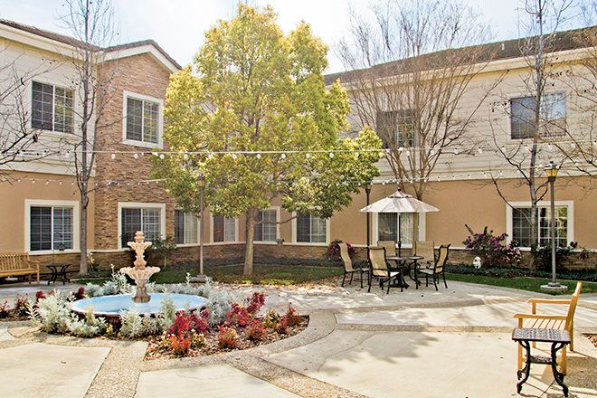 A peaceful courtyard featuring a fountain, outdoor seating, and lush landscaping.