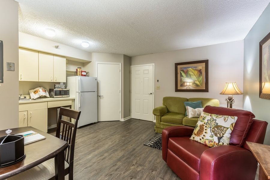 A cozy living room with a kitchenette featuring a green and red sofa, dining table, and modern appliances.