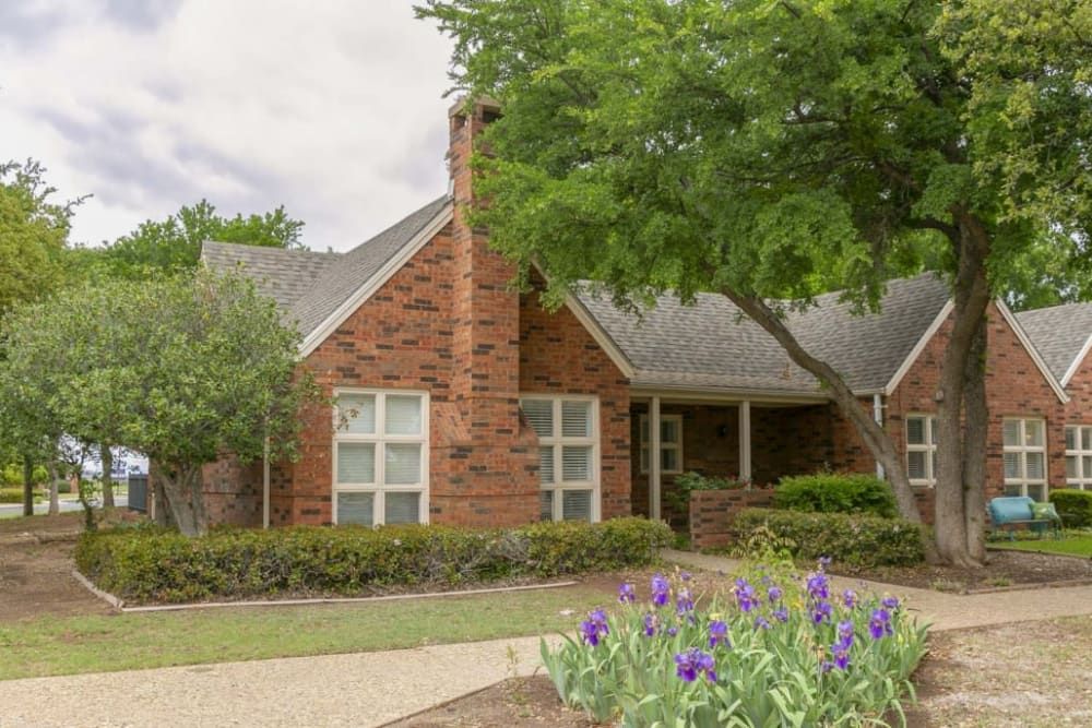A brick house with well-maintained landscaping and a tree-lined front yard.