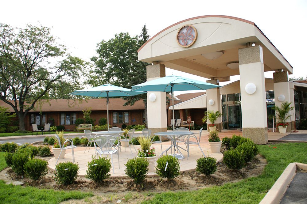 A building entrance with outdoor seating and umbrellas on a landscaped patio.