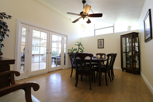 A cozy dining area featuring a wooden table with chairs, illuminated by natural light and complemented by a ceiling fan.