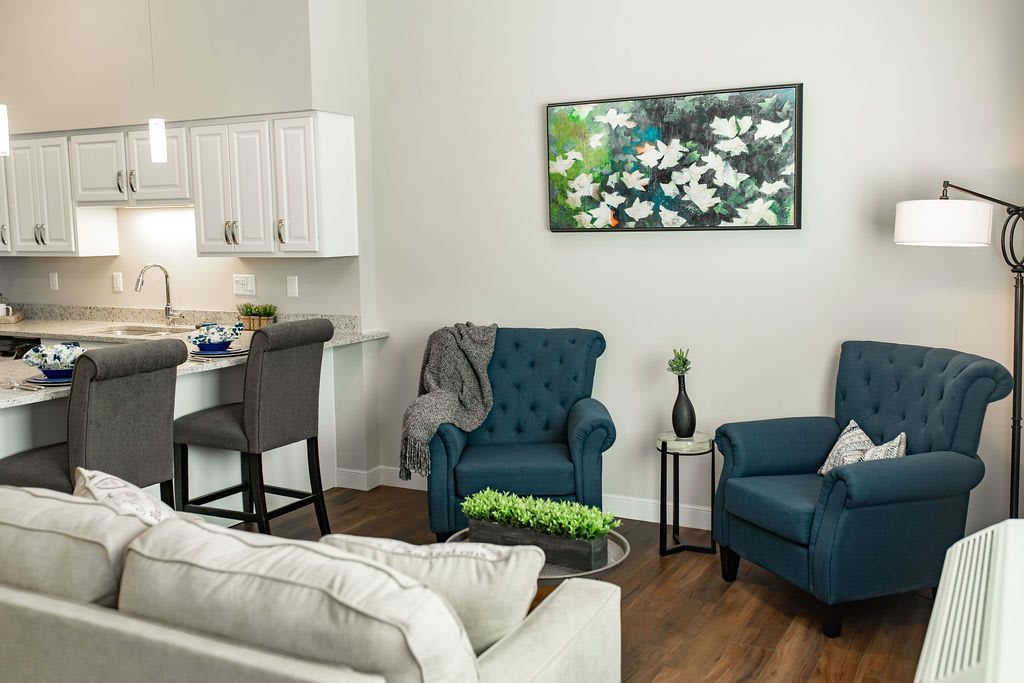 A cozy living room with blue armchairs, a beige sofa, and floral artwork on the wall.