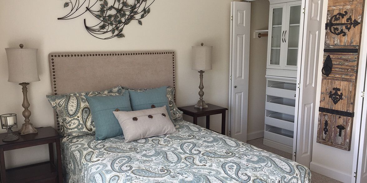 A cozy bedroom with a patterned bedspread, a bedside lamp, and an open closet.