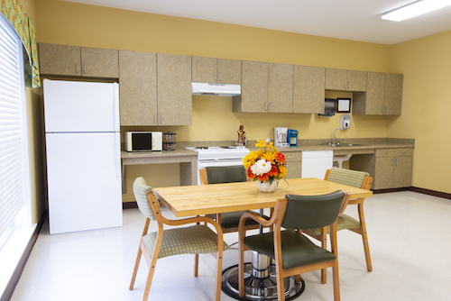 A modern kitchen and dining area featuring a wooden table with four chairs, surrounded by essential kitchen appliances.