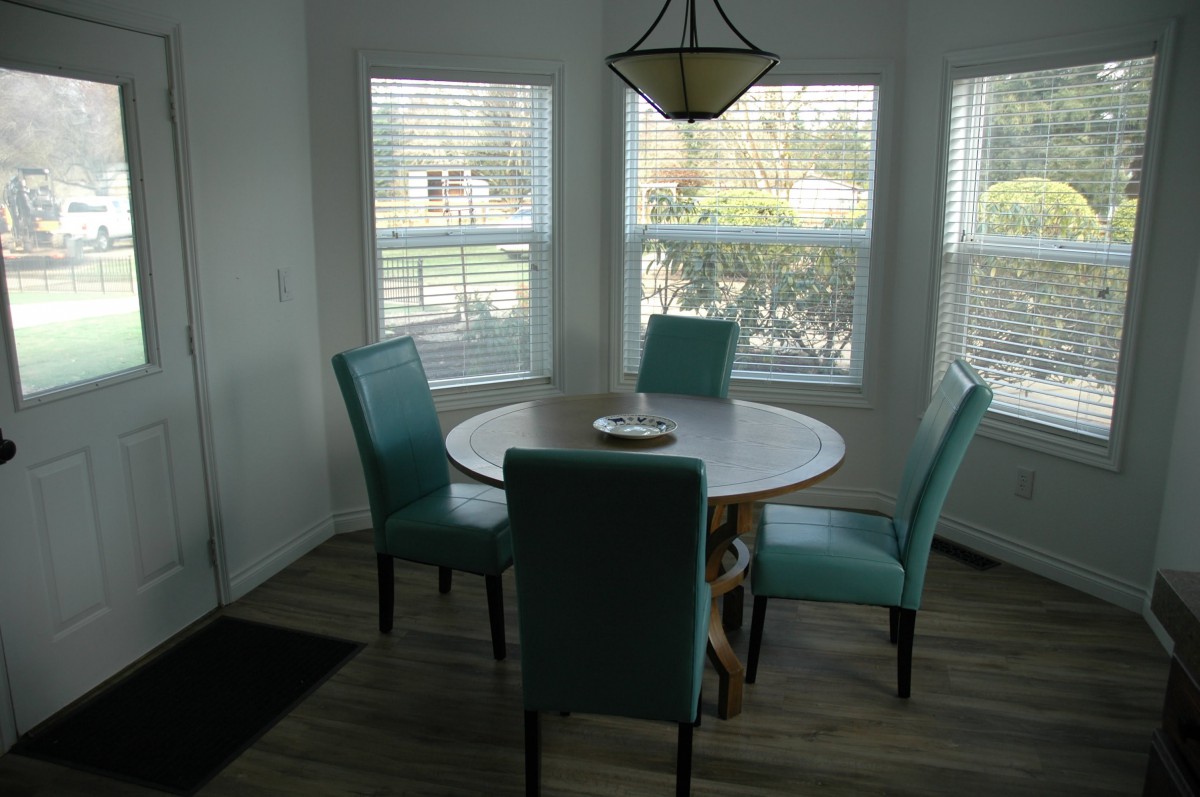A cozy dining room with a round table and teal chairs, illuminated by natural light from the windows.