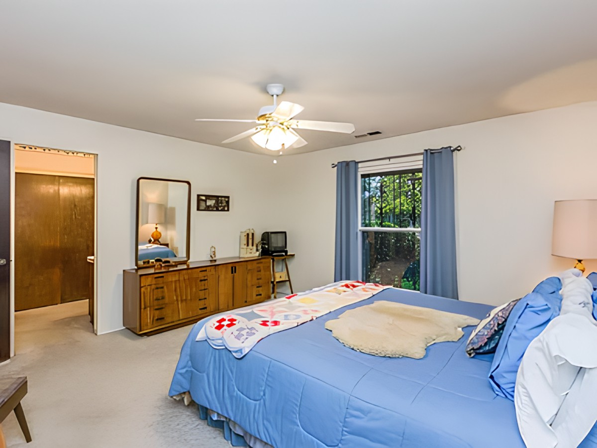 A cozy bedroom with a blue-themed decor, featuring a bed, dresser, mirror, and ceiling fan.
