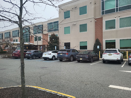 A view of a commercial building with a parking lot filled with cars, surrounded by trees.